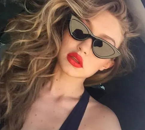 Supermodel Gigi Hadid posing for a picture on Instagram wearing black cat-eye glasses with red lipstick and a black shirt