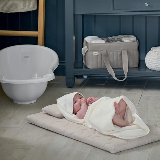 A baby wrapped in a blanket lying on a mat, with furniture nearby.