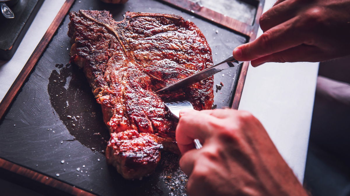 A person slicing a cooked steak on a cutting board.