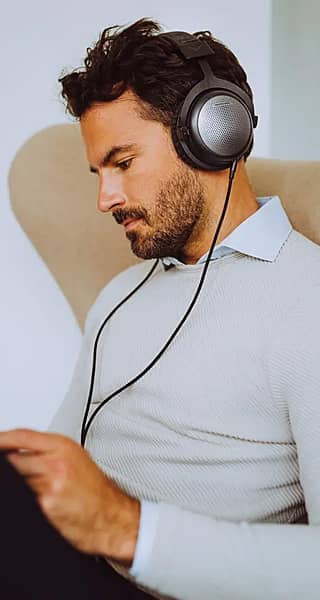 Man wearing wired headphones, sitting comfortably while listening to music.