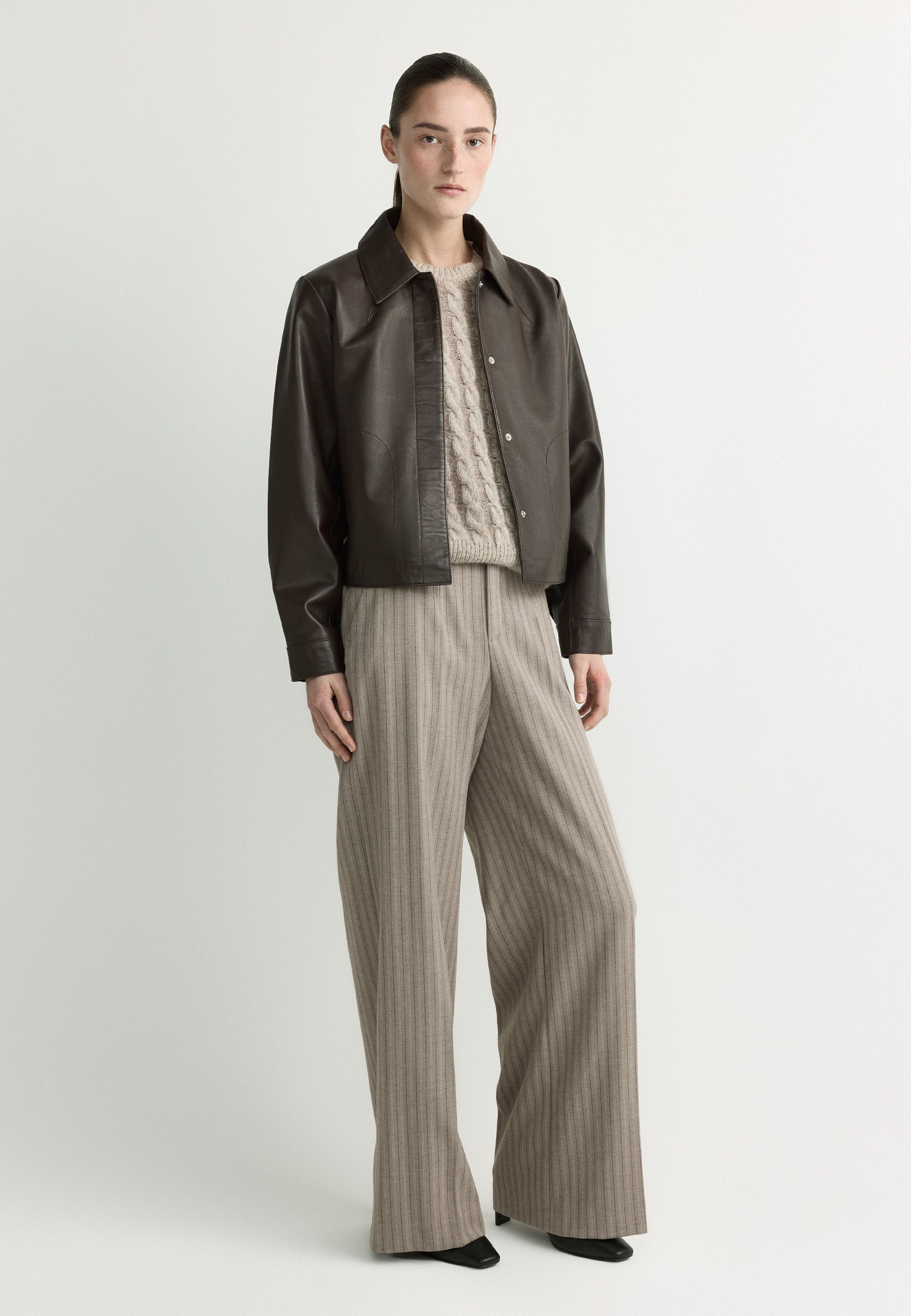 Person wearing a brown jacket and striped pants, standing against a neutral background.