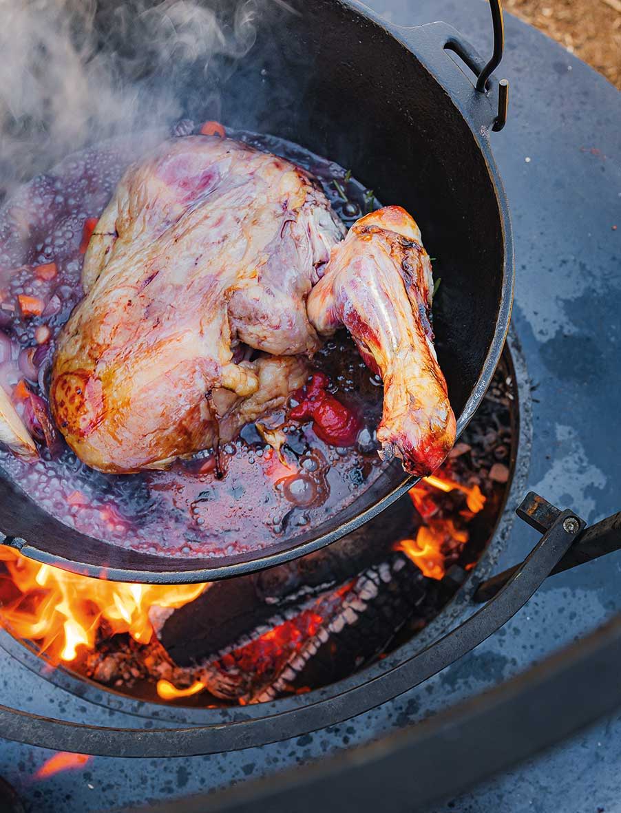 A chicken cooking in a pot over an open fire.