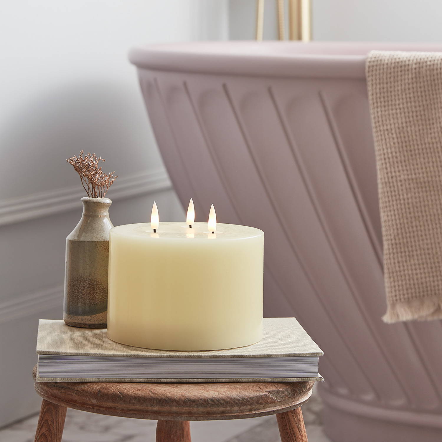 A 3 wick LED candle on a stool in front of a bath tub.