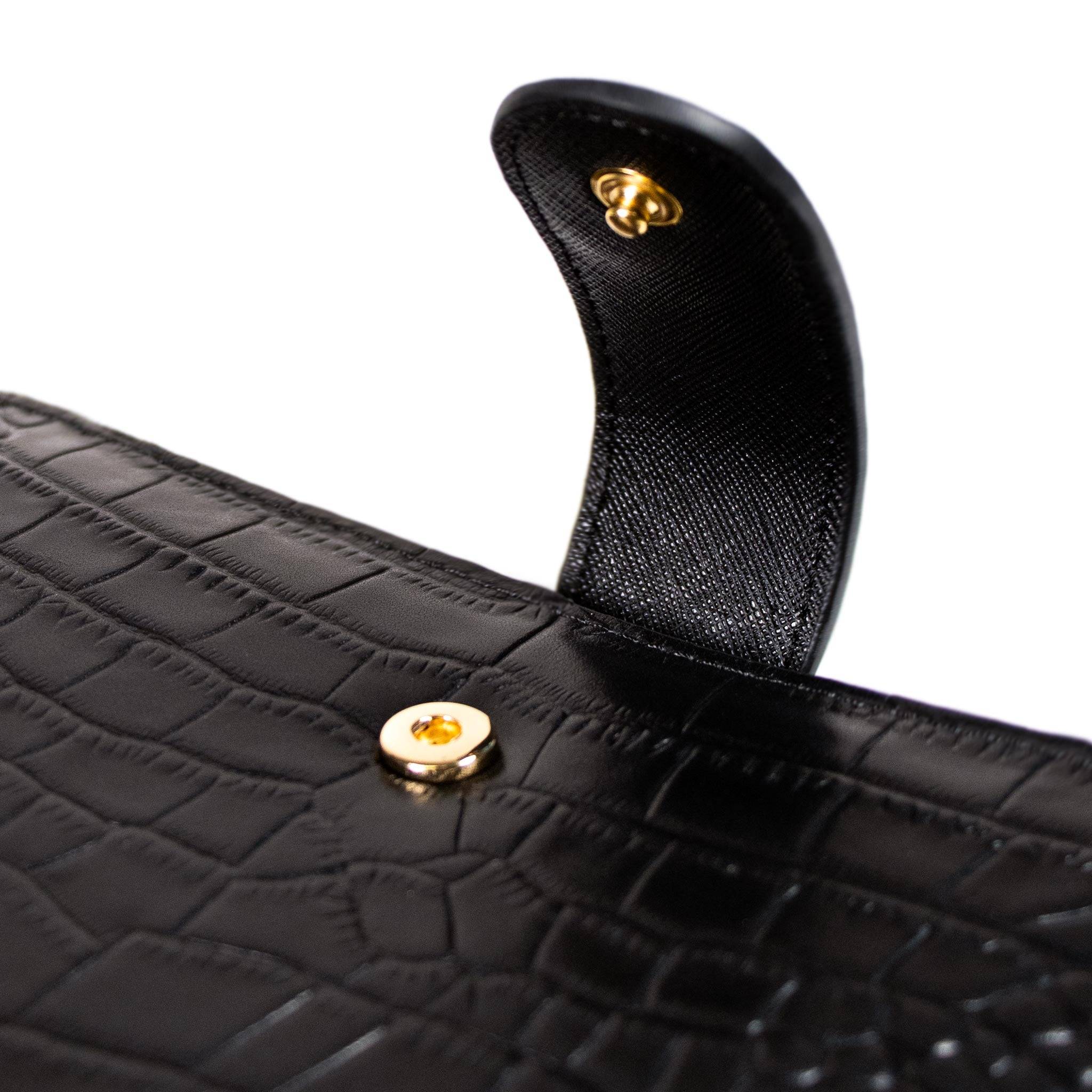 Close up image of gold metal snap closure on black croc leather agenda cover