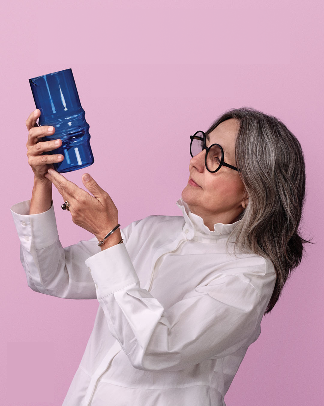 Woman with glasses holding a blue object against a pink background.