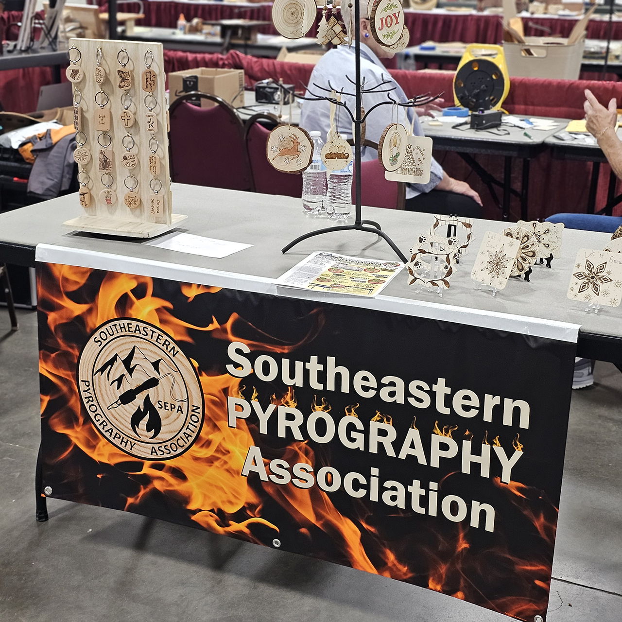 Table displaying pyrography art with a sign for Southeastern Pyrography Association.