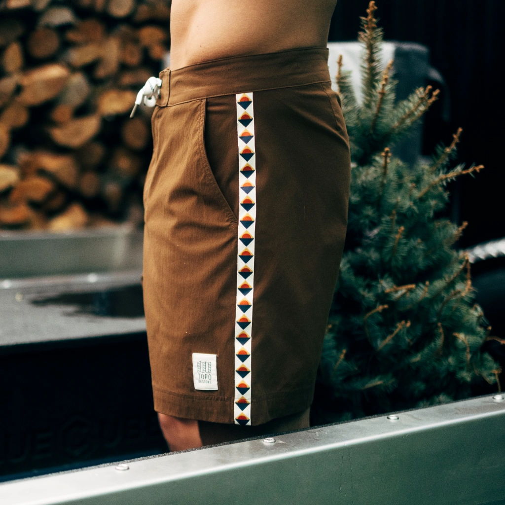 Person wearing brown shorts with decorative side pattern, standing near a tree.