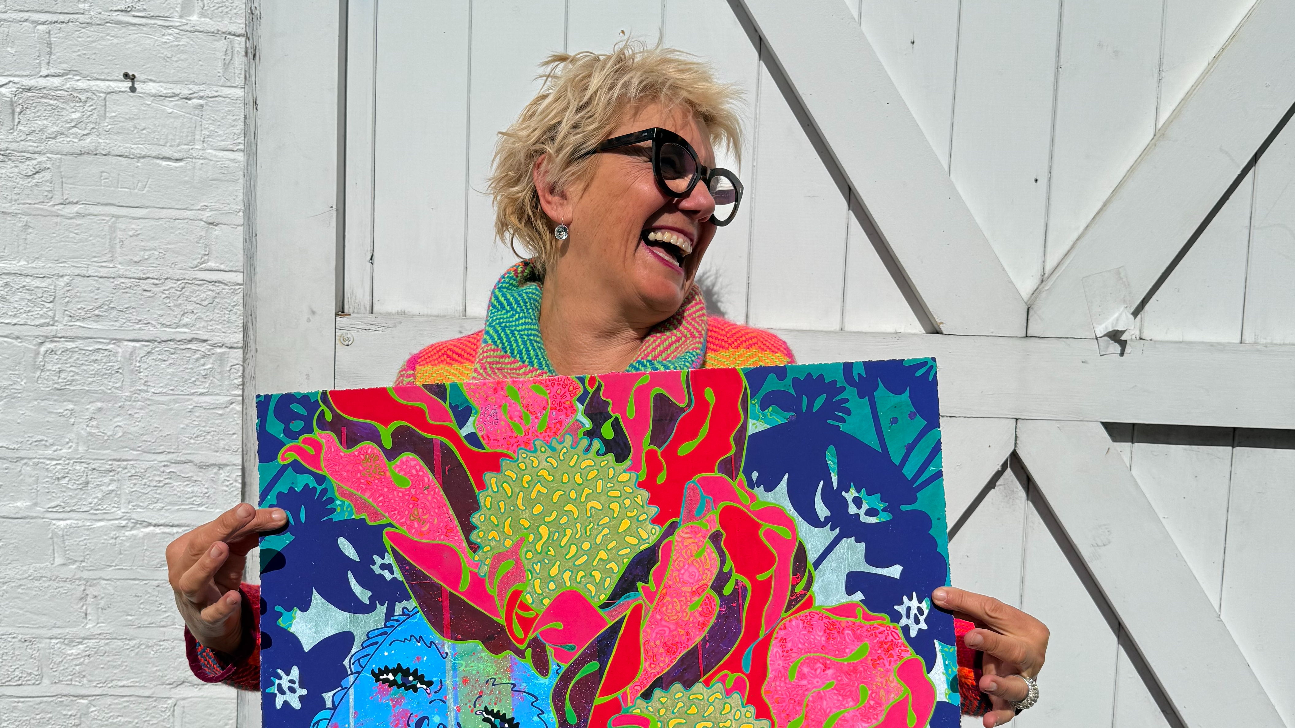 Artist Louise Dear Laughing and holding one her of new artworks in the Pursuing Pleasure Collection.