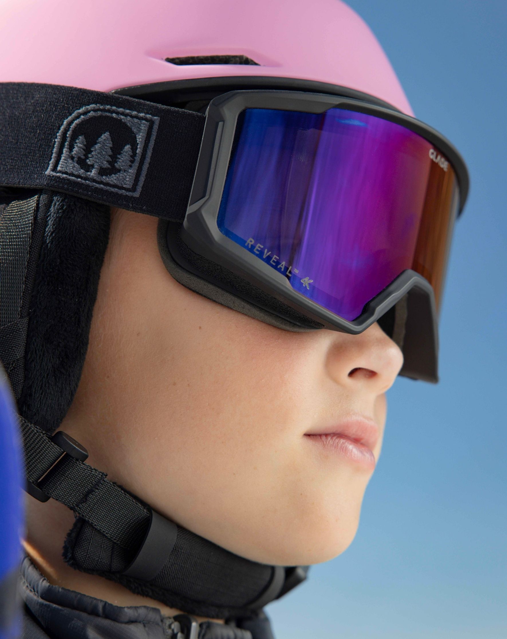 Child wearing a pink helmet and ski goggles against a clear blue sky.