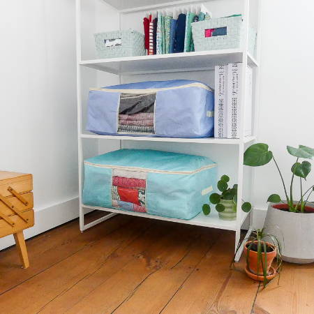 Two quilt storage bags on a shelf in a craft room