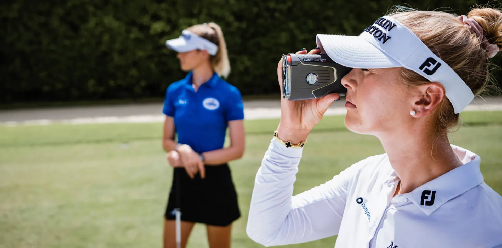 A golfer holding the Bushnell Pro X3 rangefinder to her eye while another woman golfer looks at her target on the golf course