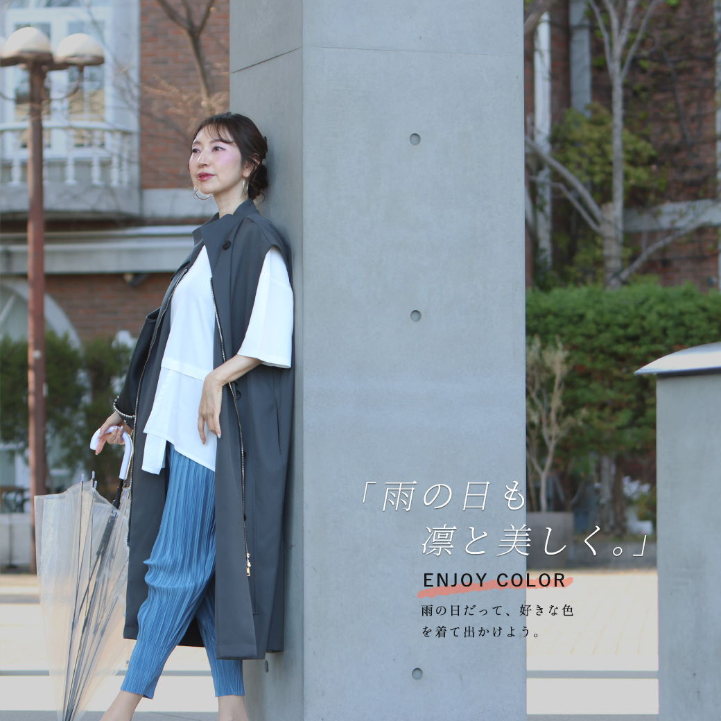 A woman in casual attire poses beside a pillar outdoors.