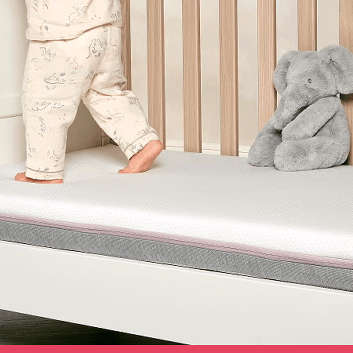 Child standing in crib next to a stuffed elephant toy.