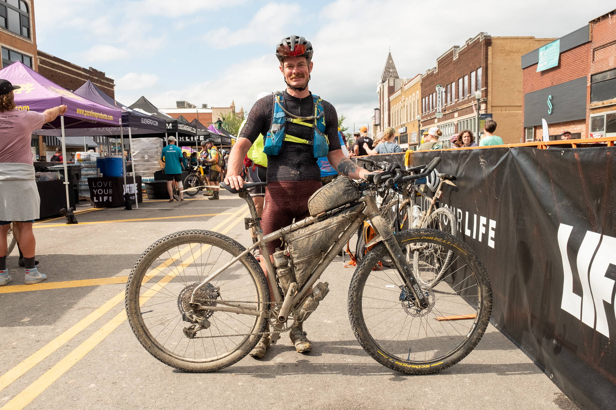 Dylan Morton stands at the finish line of the 2022 Unbound Gravel XL with his fully-loaded Otso Fenrir Stainless bicycle.
