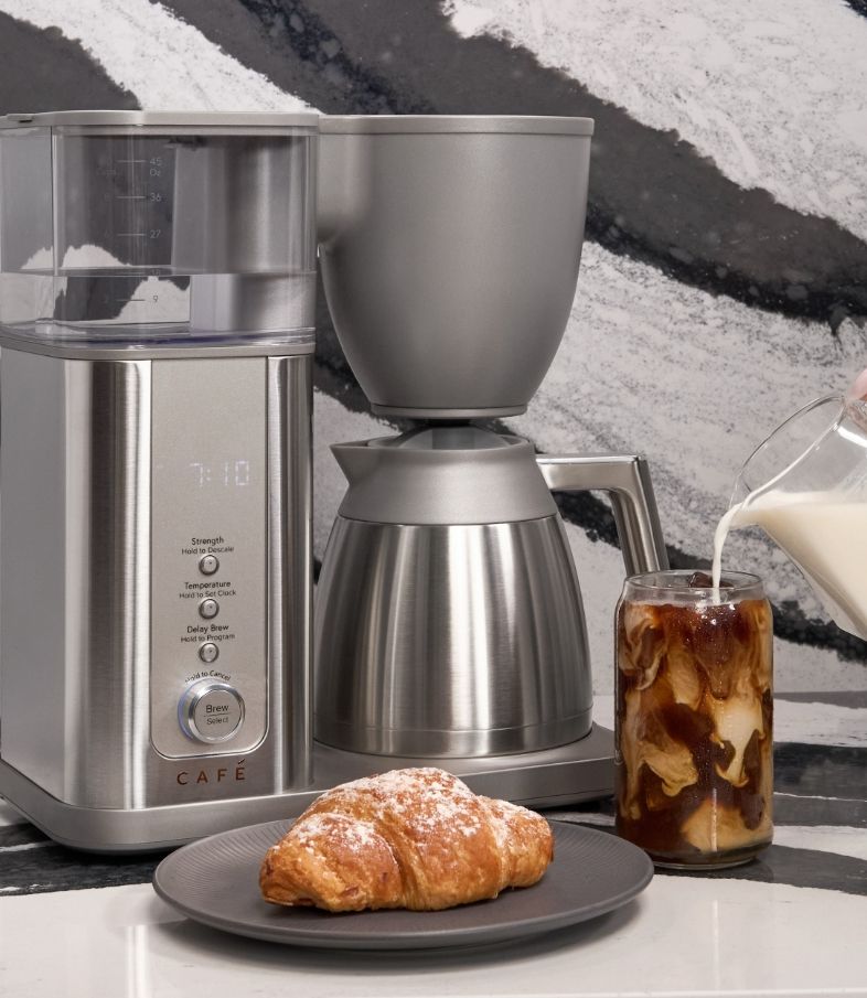 Coffee maker, ground coffee, croissant, iced coffee with milk, modern kitchen setting.