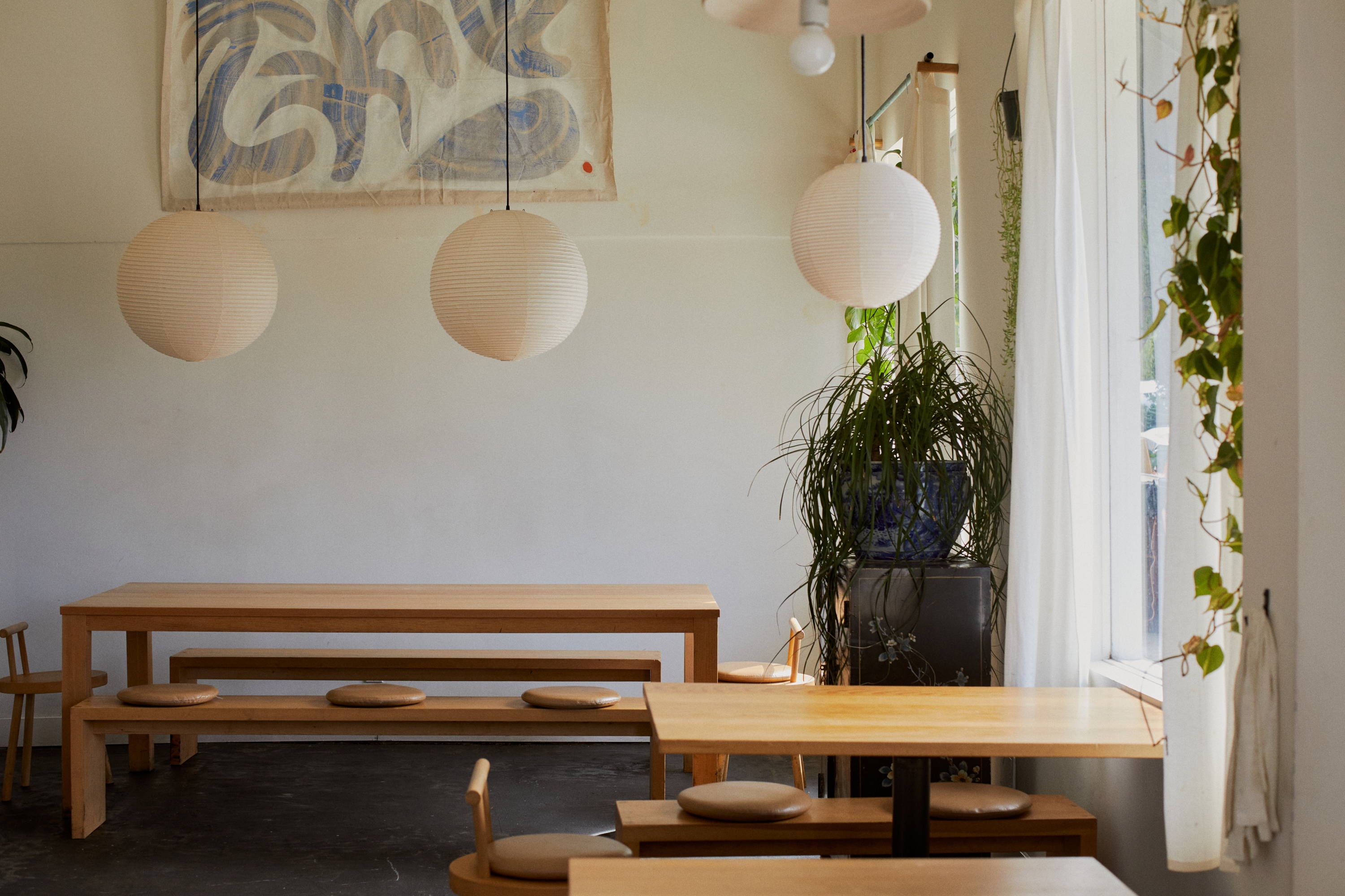 Dining area with plants, cool lighting, warm wood tables, benches with cushions