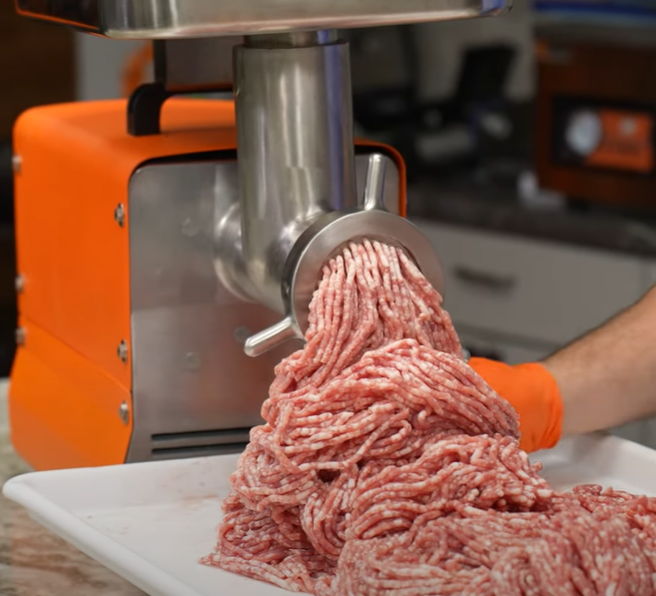 Meat being ground from a meat grinder into a pile on a plate.