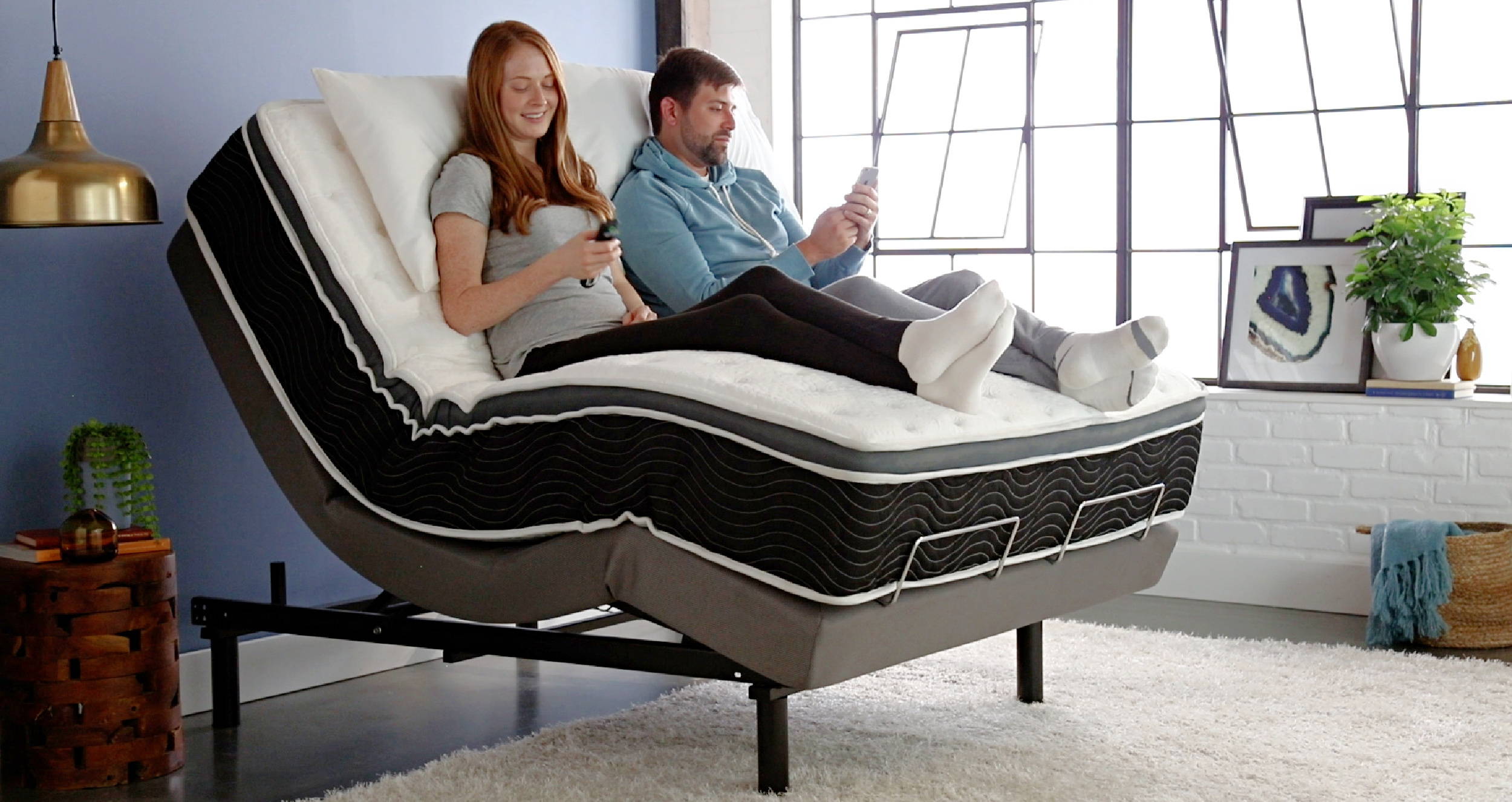 A couple relaxing on a mattress with the iTilt adjustable base in a lounge position, watching TV.