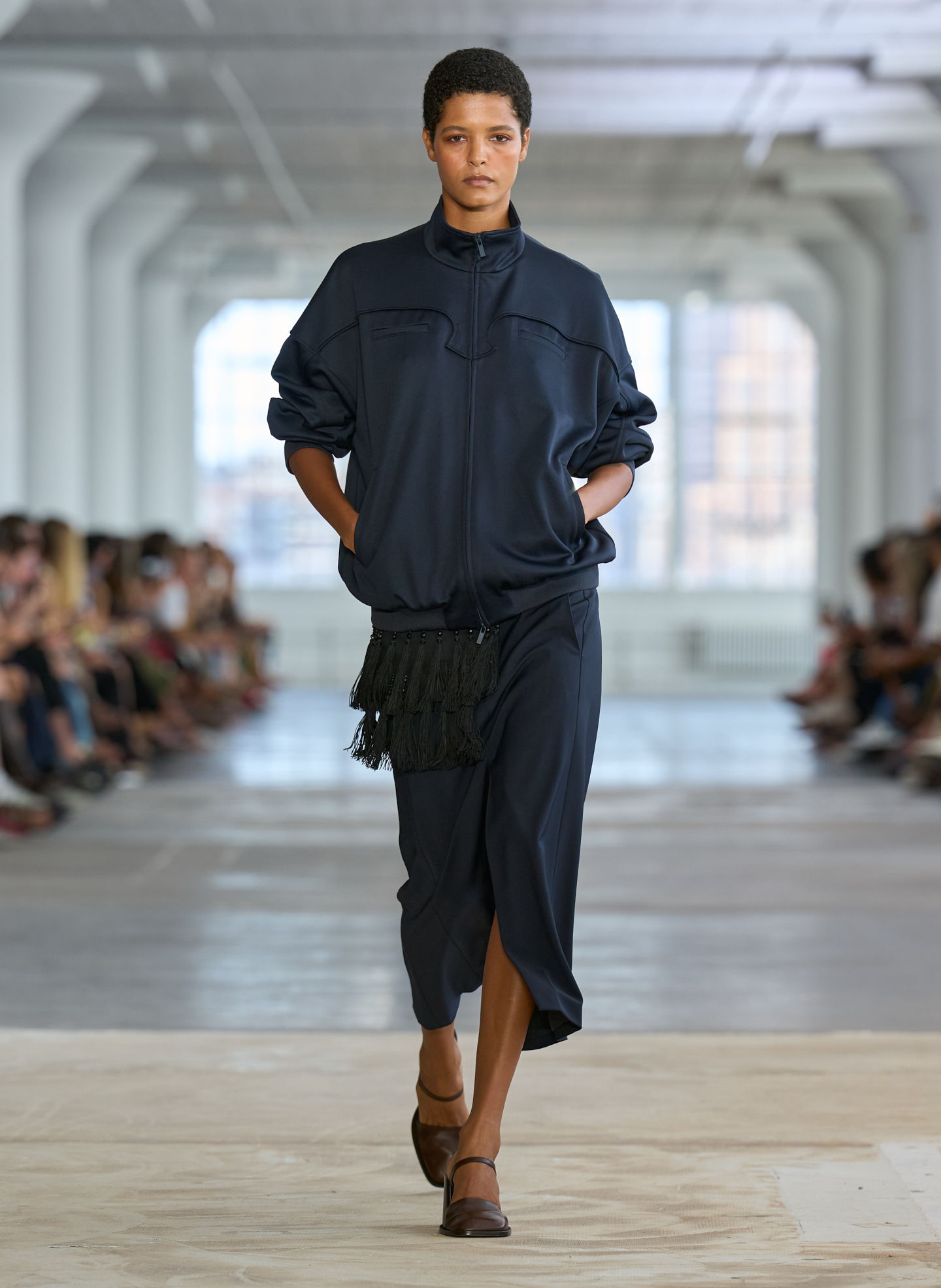 Model walking down runway in navy outfit during fashion show.