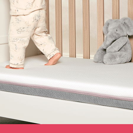 Child standing in crib next to a gray stuffed elephant.
