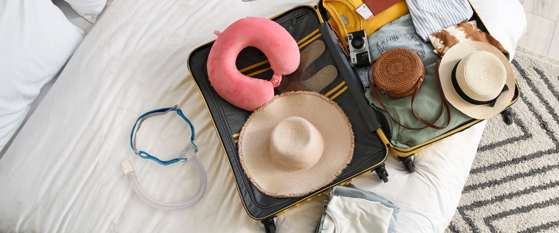 A suitcase opened on a bed with various travel accessories and hats.
