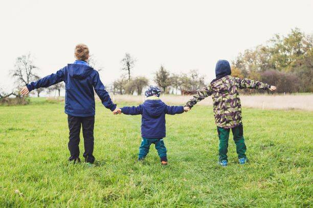 Three Children Holding Hands Standing On Grass