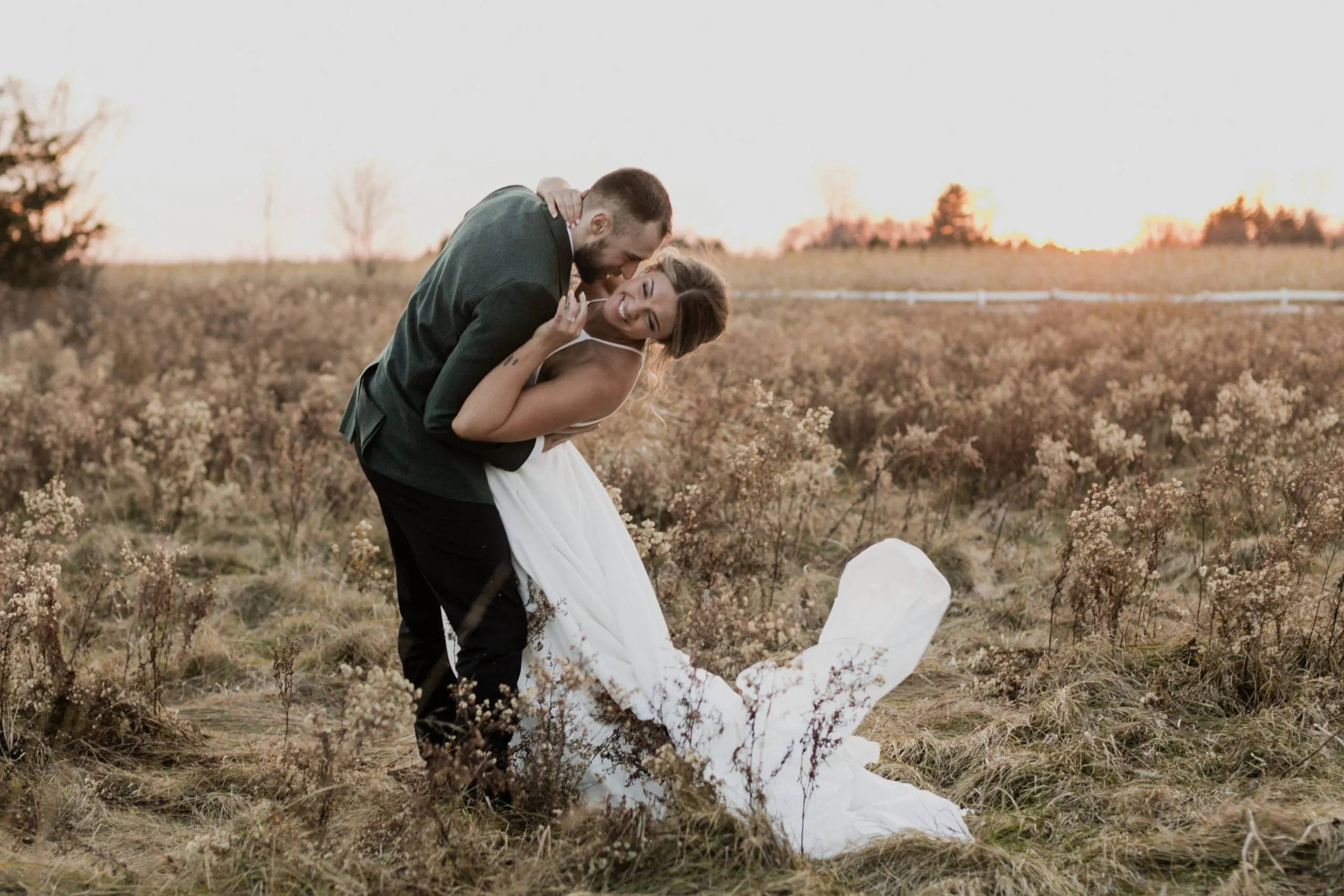 Couple hugging in field wearing a suit and wedding dress