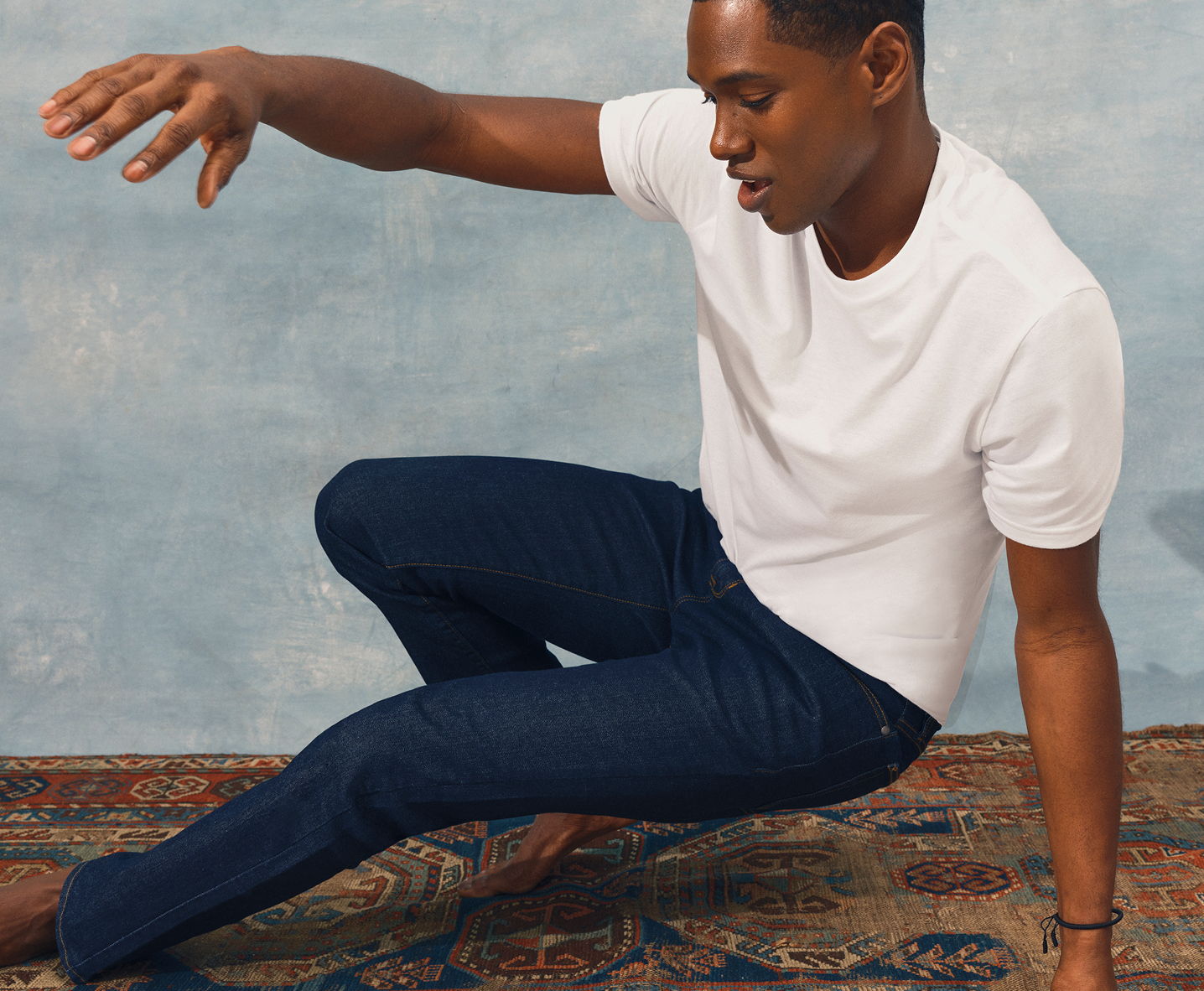 Person in a white shirt and blue jeans poses on a rug.