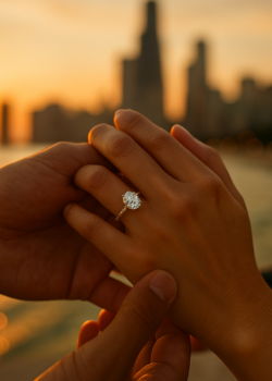 A close-up of a woman's hand wearing a diamond engagement ring as her partner gently holds her fingers.