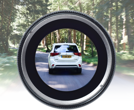 White car driving on a forest road through a camera lens.
