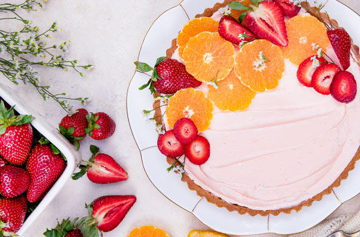 A dessert tart topped with strawberries and pixie tangerine slices on a white plate.