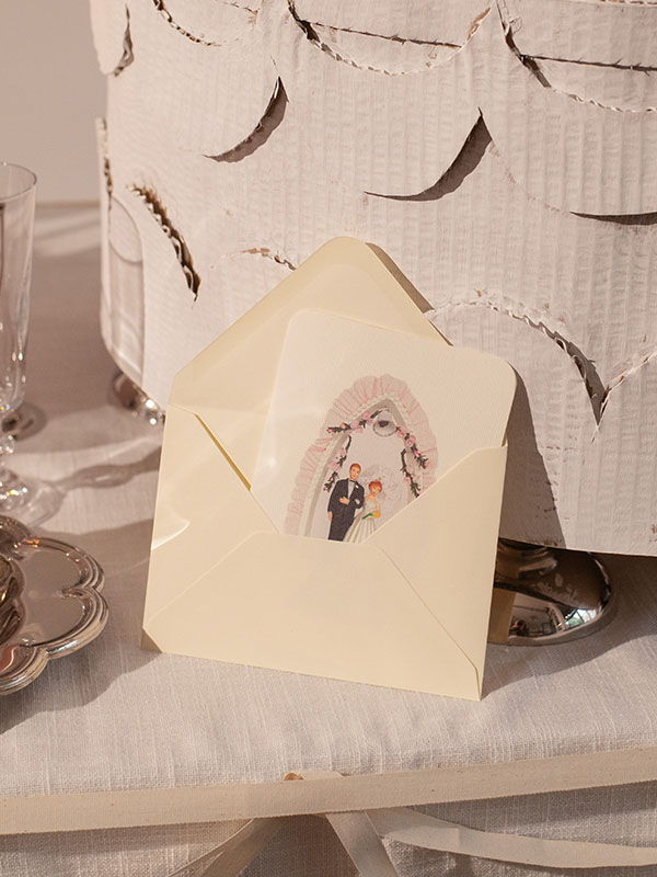 An open envelope with a wedding illustration inside, on a decorative table.