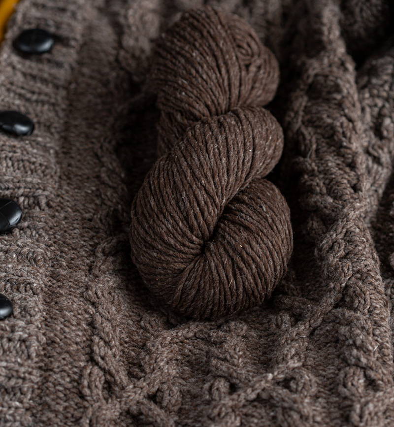 A skein of Brooklyn Tweed Quarry in color Otter sits on a chunky knit cabled cardigan.