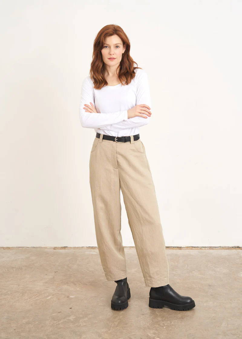 A model wearing a white long sleeved top with cream and khaki striped barrel leg trousers and black chunky chelsea boots