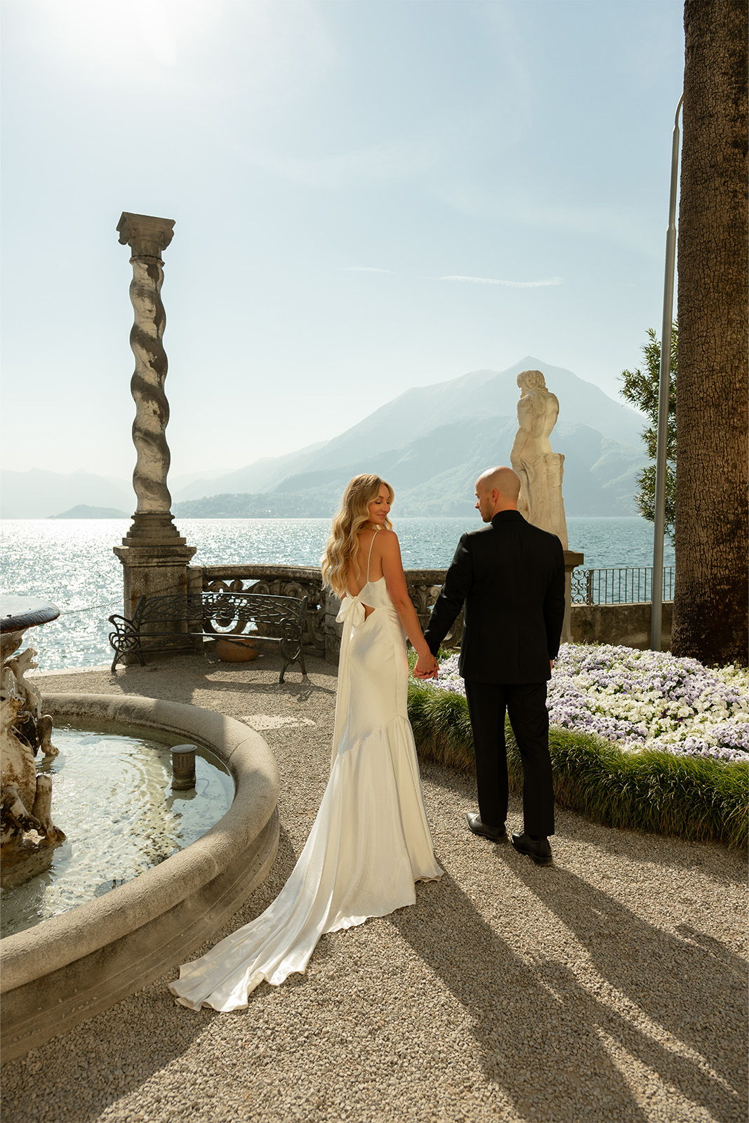 Couple holding hands by a lake with mountains in the background.
