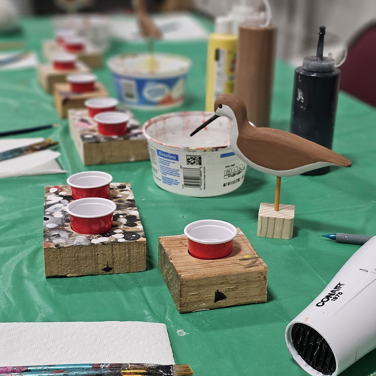 Art supplies and a painted bird on a green table.