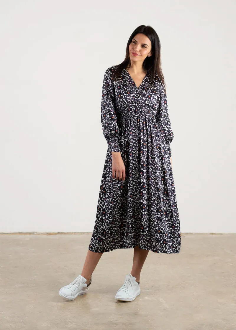 A model wearing an inky blue floral dress with a floral design, long sleeves and a midi length.
