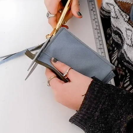 hand showing how to clip off excess fabric and a long zipper