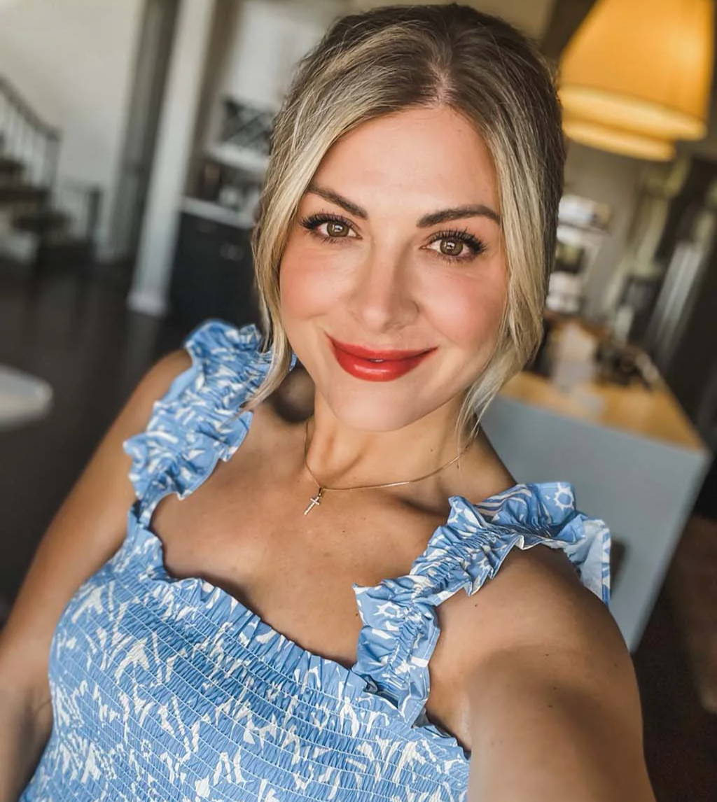 Woman with blonde hair wearing a blue dress, smiling in a cozy interior.
