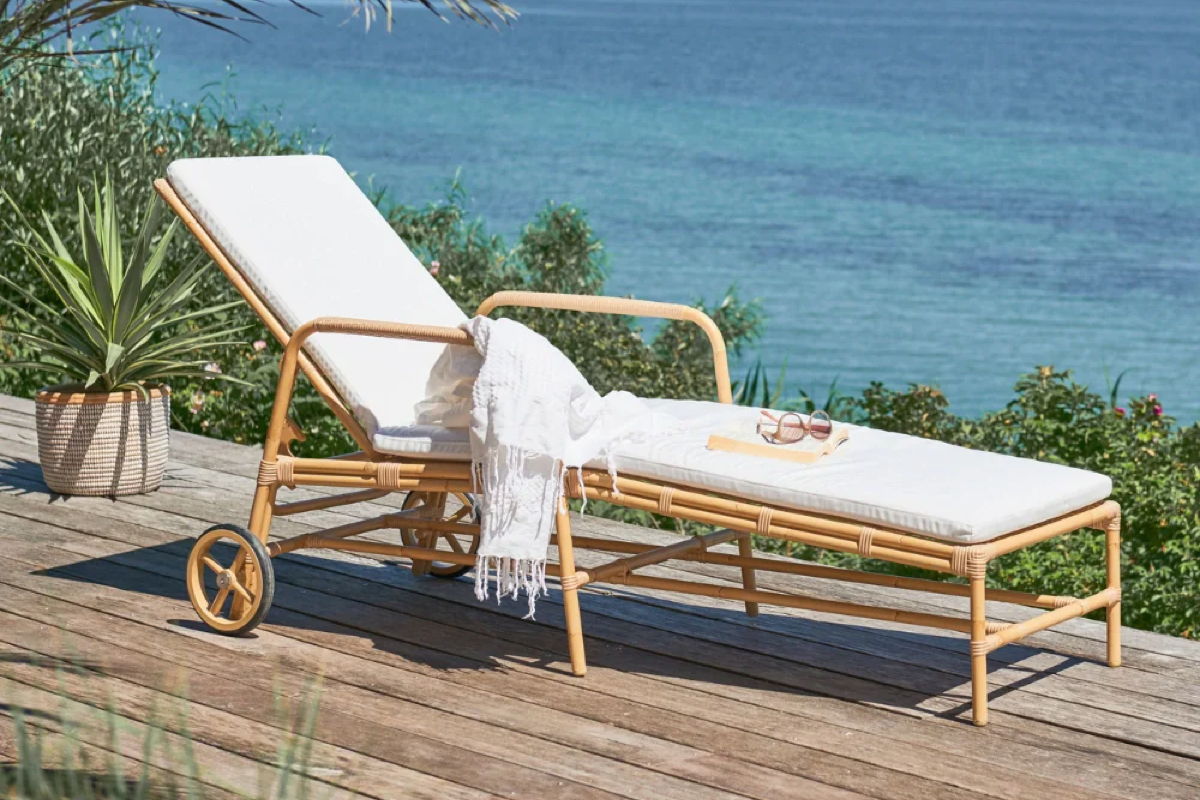 Outdoor sun lounger with white cushion on a coastal deck with ocean views.