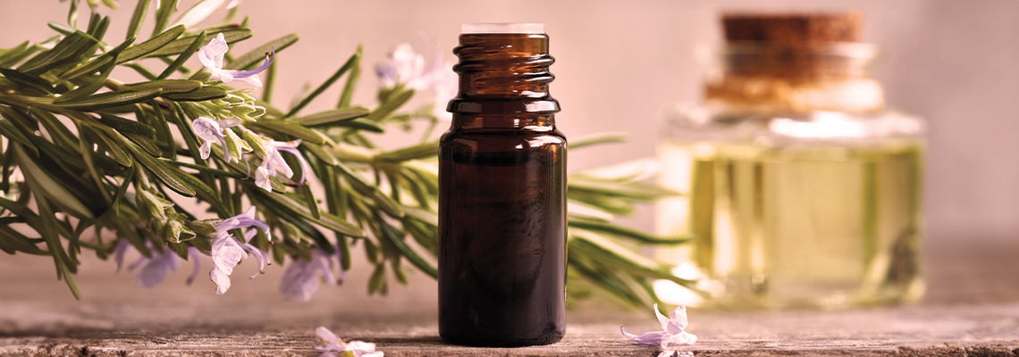 Brown essential oil bottle with rosemary and another glass bottle in the background.