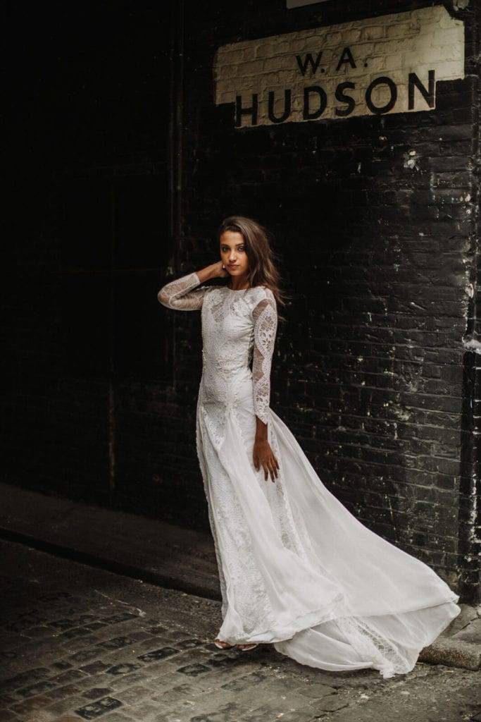 Grace Loves Lace bride wearing the Inca wedding dress against painted black brick wall 
