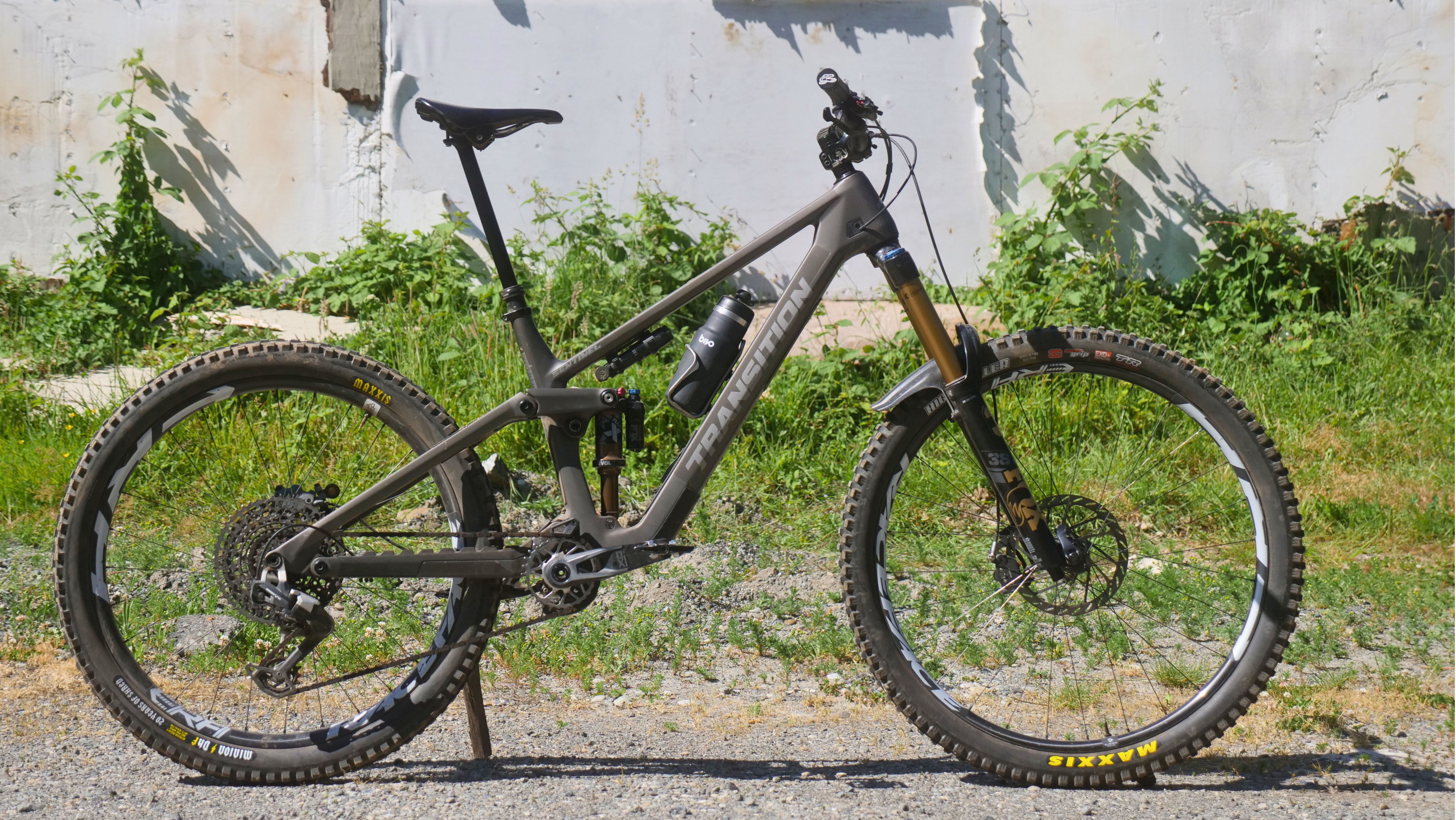 A mountain bike parked on a gravel surface with greenery in the background.