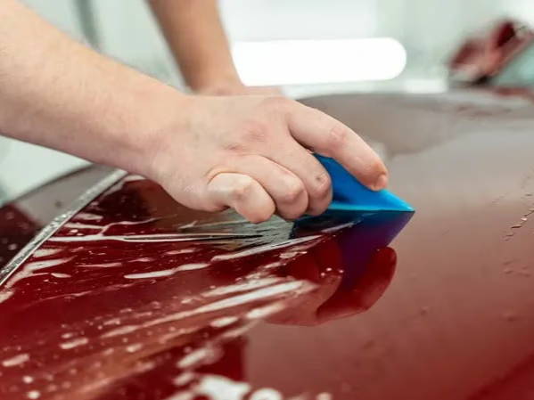 PPF installation — squeegee on red Tesla