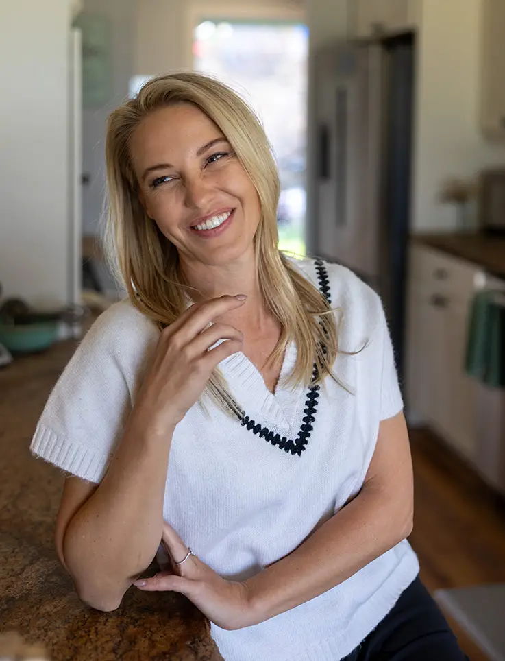 Smiling woman in a white sweater, sitting at a kitchen counter.