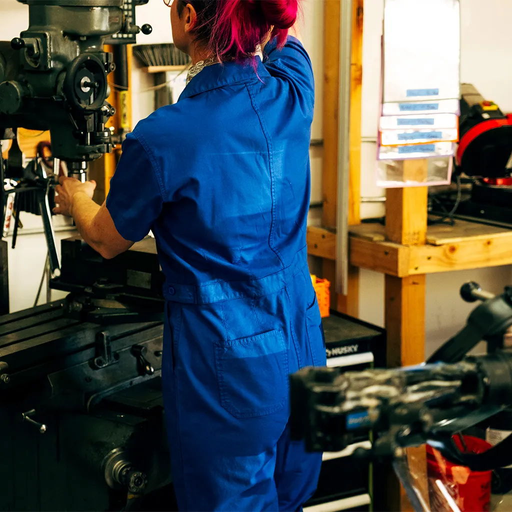 Person in blue jumpsuit working in a workshop with machinery.