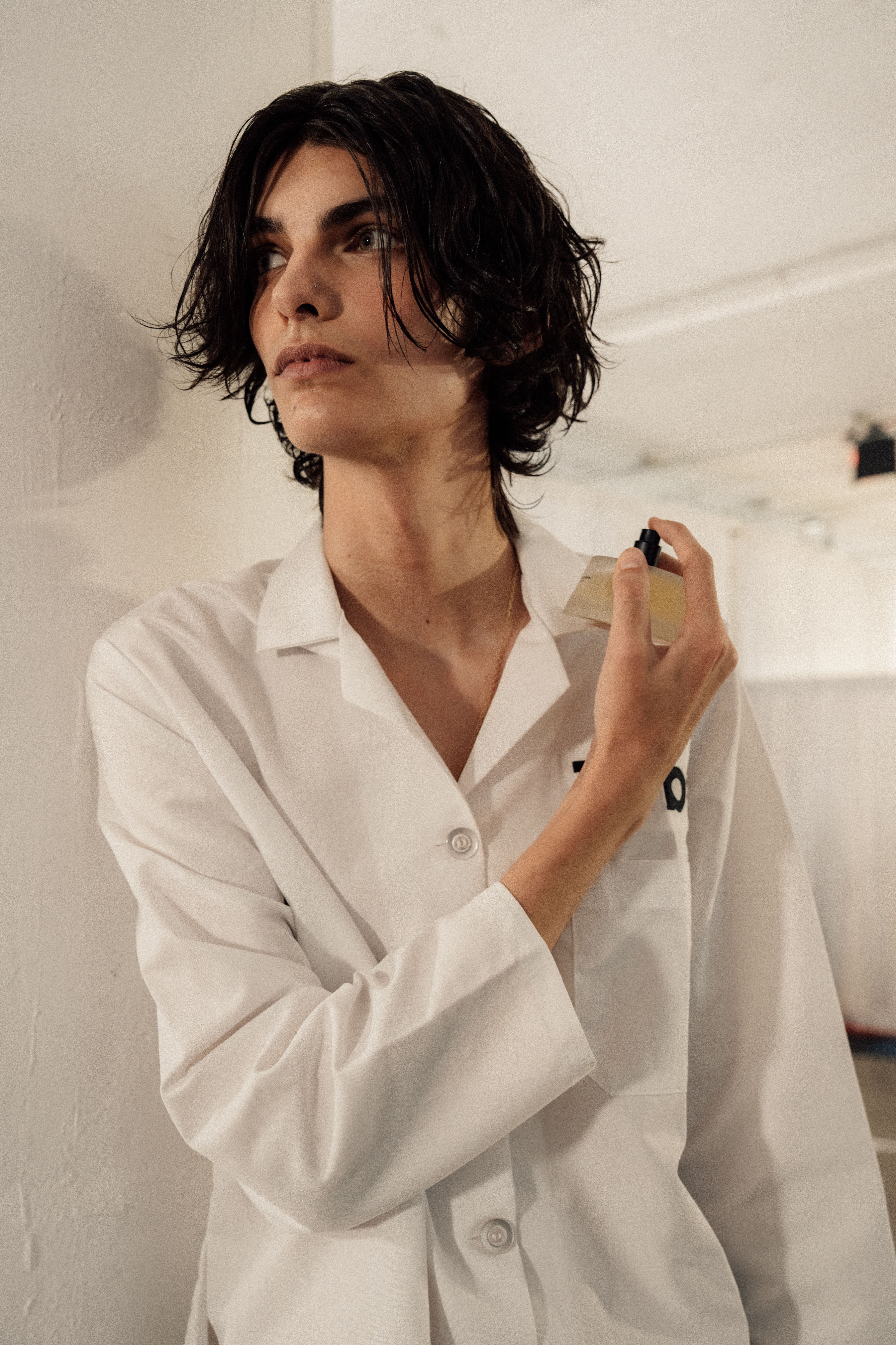 Person in a white lab coat applying perfume in a minimalist setting.