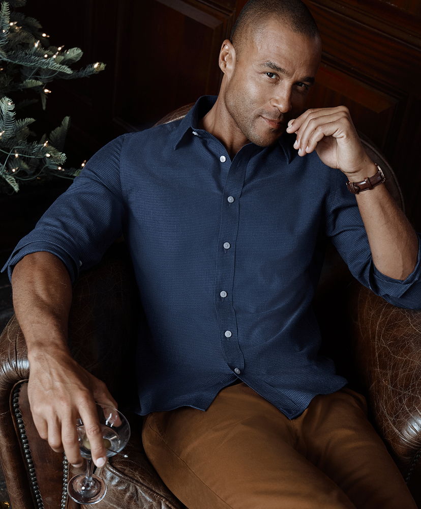 Man in a blue shirt sitting on a leather chair, holding a glass.