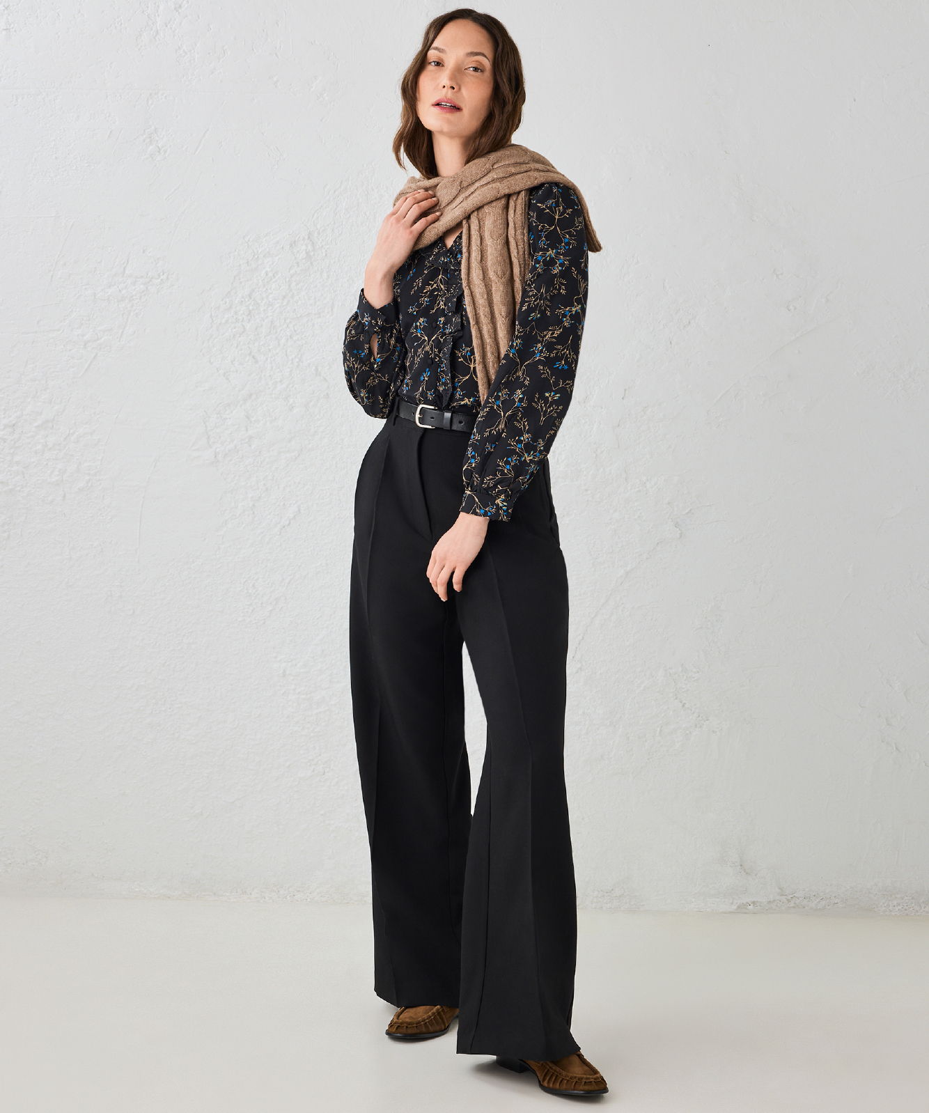 Woman in floral top and wide-legged pants, holding a scarf.