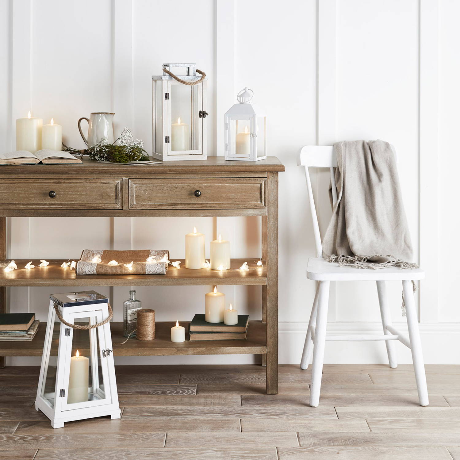 Illuminated candles and lanterns displayed on wooden cabinet.